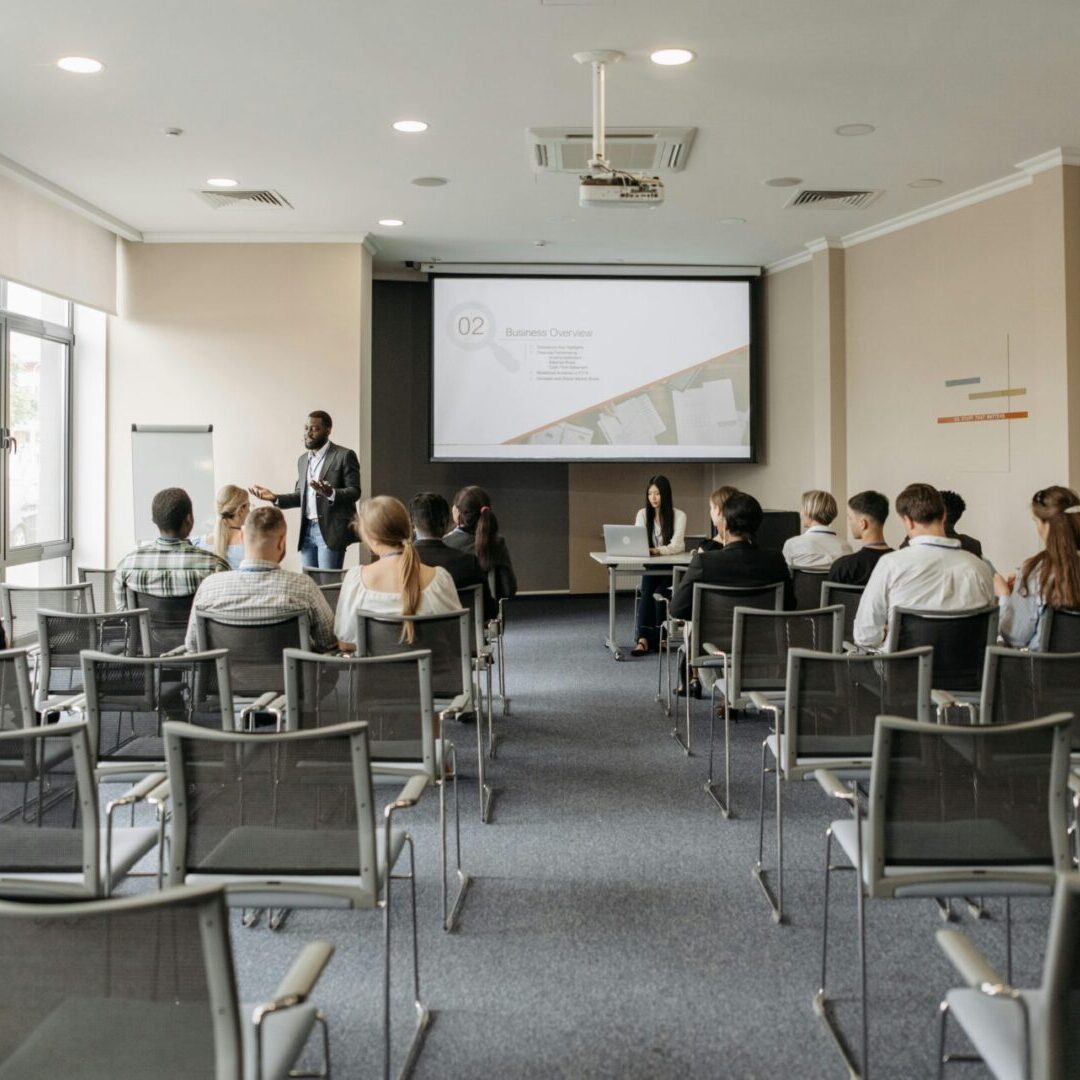 A presenter speaks to an attentive audience in a modern conference room.